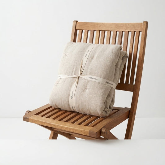 Folded natural color thick linen blanket on a wooden folding chair with the name Peplos Linen written on a ribbon