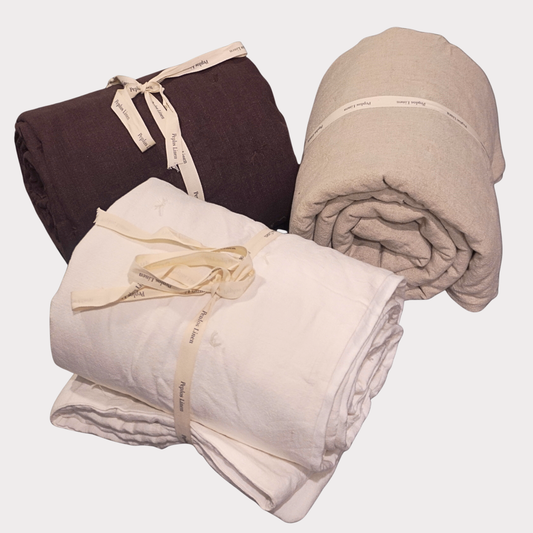 Three rolled up linen quilts in the color ivory, chocolate and natural beige