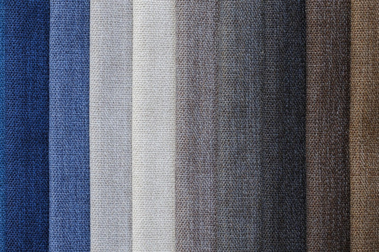 Close-up of textured linen fabric swatches arranged side by side in a gradient, ranging from deep blue to light beige, gray, and various shades of brown