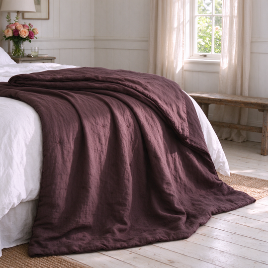 Image of a brown linen quilt on a white bed next to an open window