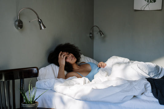 Person lying awake in bed with a hand on forehead, struggling with overheating and discomfort during sleep.