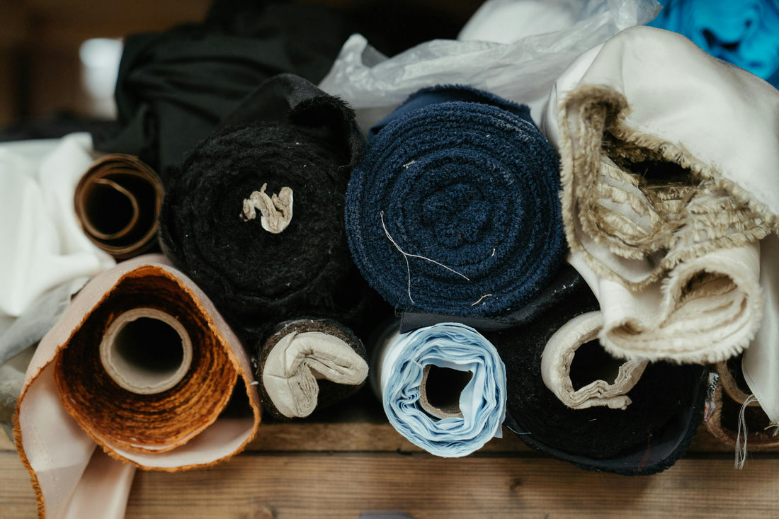 A tightly arranged collection of fabric rolls in varying textures and muted tones—linen.