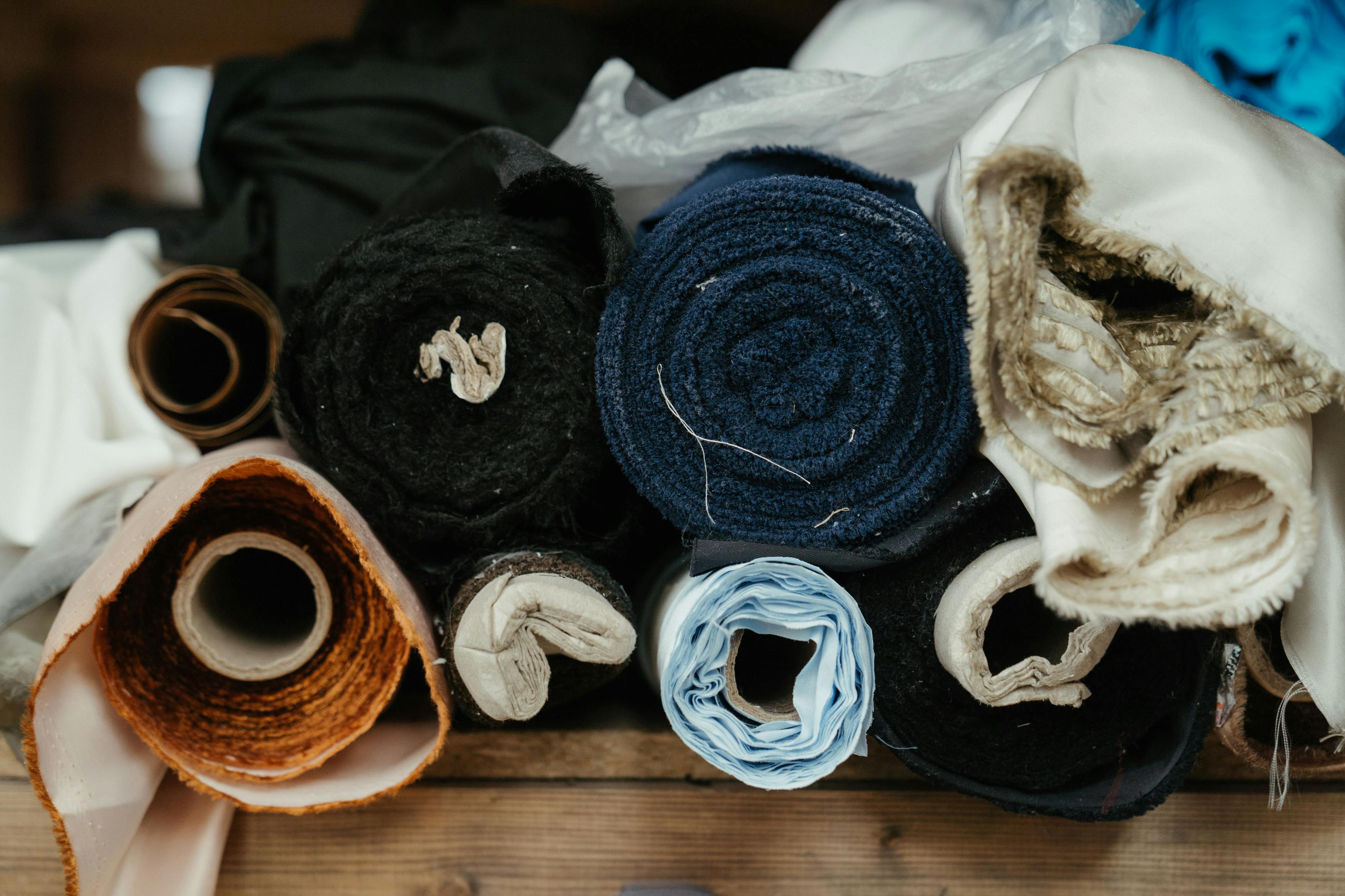 A tightly arranged collection of fabric rolls in varying textures and muted tones—linen.