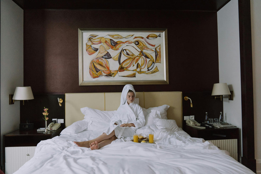 Women sits on hotel bed win robe with breakfast in bed. 