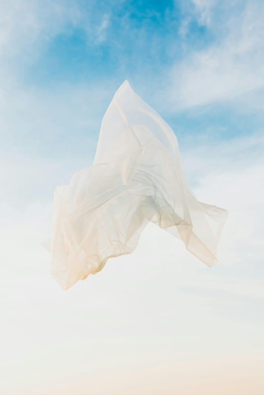 Soft linen fabric billows gently in the wind against a clear blue sky, capturing movement, texture, and lightness
