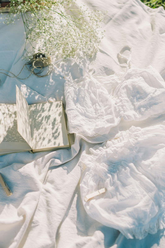 White linen fabric softly draped with a book and delicate flowers resting on top—evoking calm, texture, and timeless elegance.