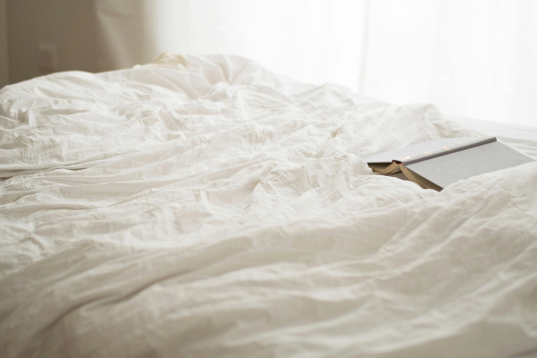 White linen quilt draped softly with a facedown open book—inviting rest, reflection, and quiet luxury