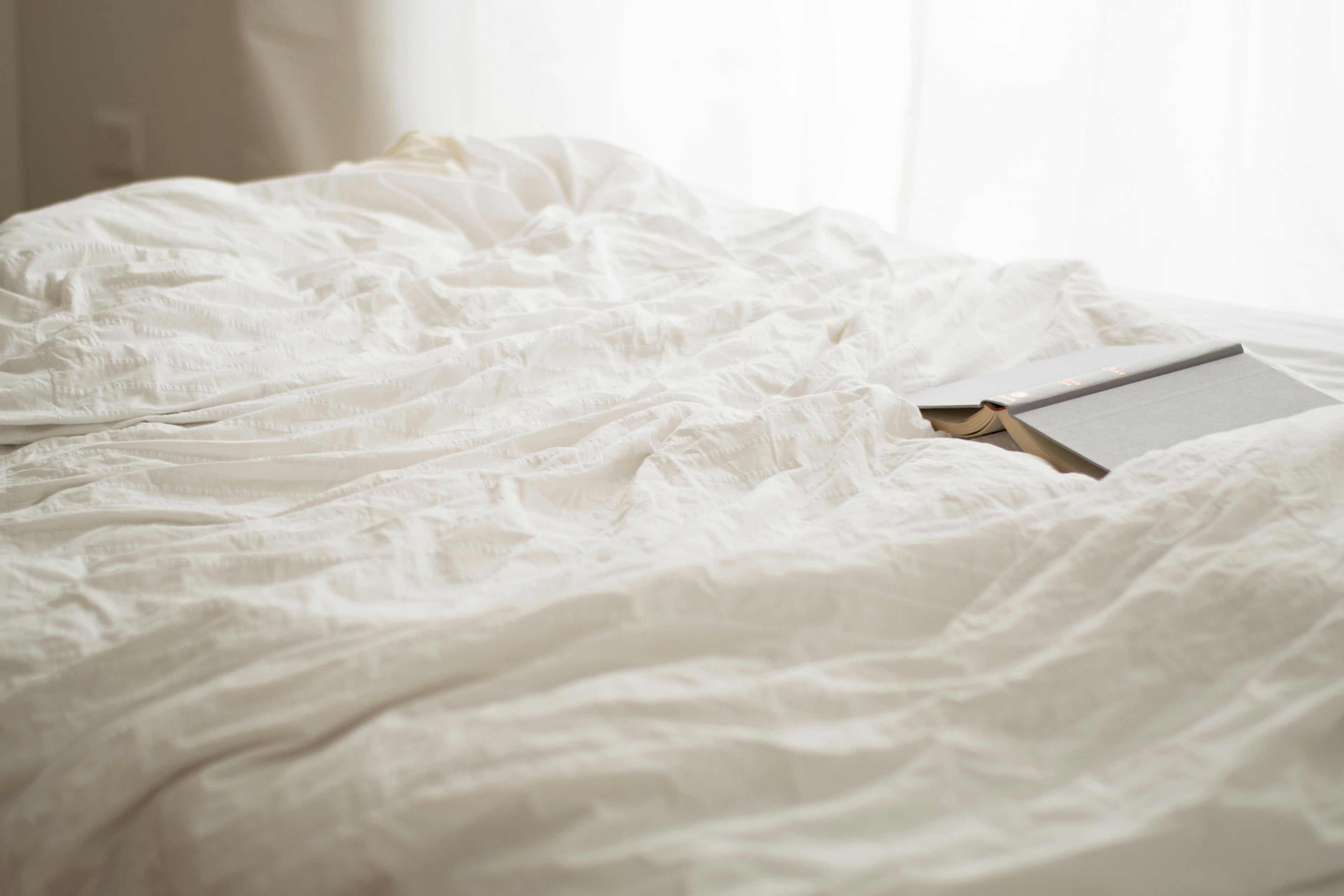 White linen quilt draped softly with a facedown open book—inviting rest, reflection, and quiet luxury