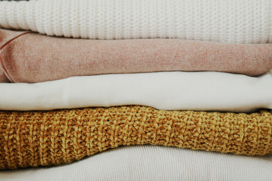 Stack of folded quilts in different weights and textures, illustrating GSM in fabric. Quilt fabrics in various thicknesses, showing examples of different GSM levels. Lightweight, medium, and heavyweight quilt fabrics stacked together to explain GSM.
