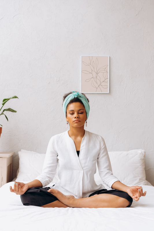 Individual seated cross-legged on a bed in a serene bedroom, symbolizing calm, balance, and restoration.