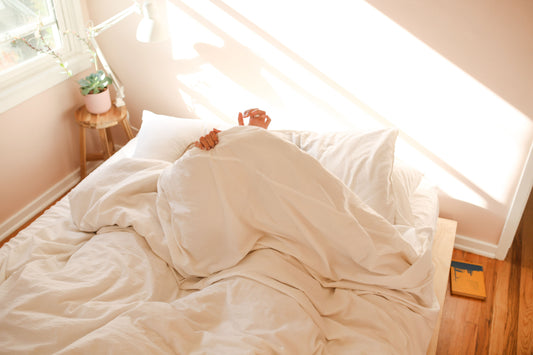 Person wrapped in a white linen quilt in a bright bedroom, showing cozy and breathable bedding for year-round comfort.