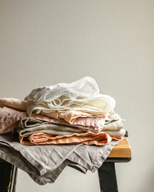 a stack of different color linen fabrics in folded on a wooden stool