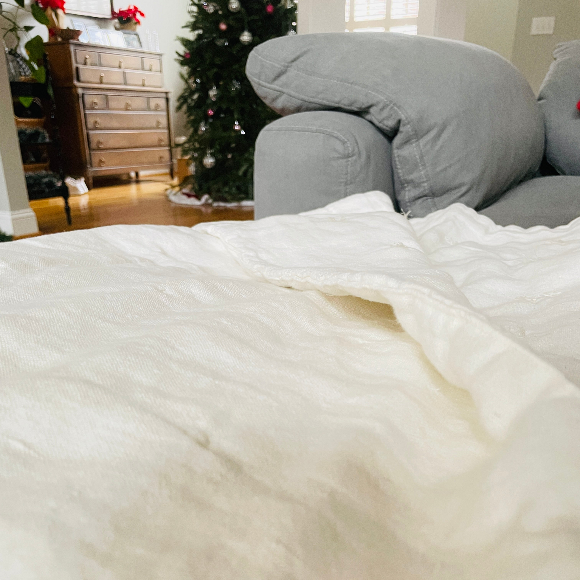 White linen quilt on a sofa with a Christmas tree and furniture in the background