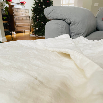 White linen quilt on a sofa with a Christmas tree and furniture in the background