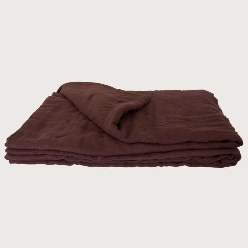 A folded dark brown linen blanket or linen quilt, displayed on a clean, solid off-white background.