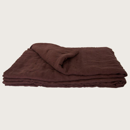 A folded dark brown linen blanket or linen quilt, displayed on a clean, solid off-white background.