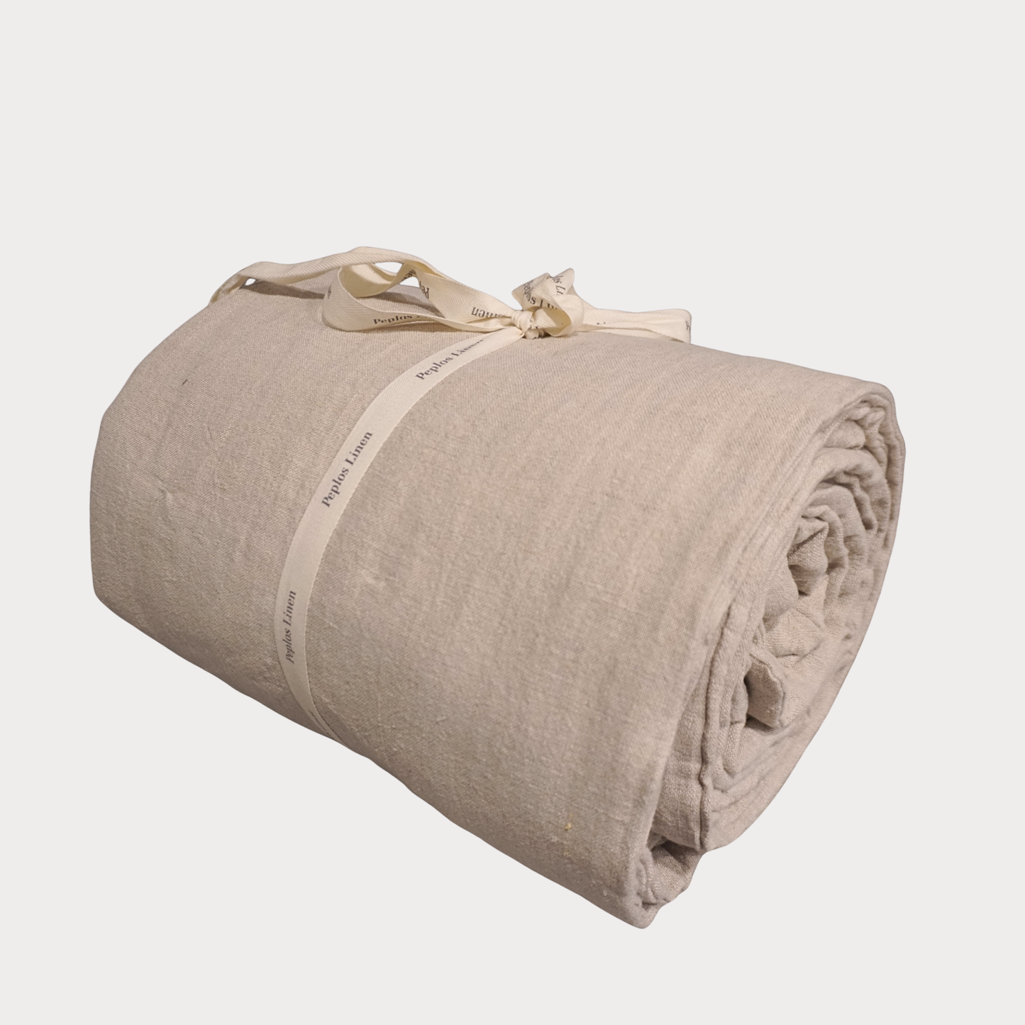 A rolled beige linen blanket tied with a cream-colored paper band and ribbon, shown on a light gray background.