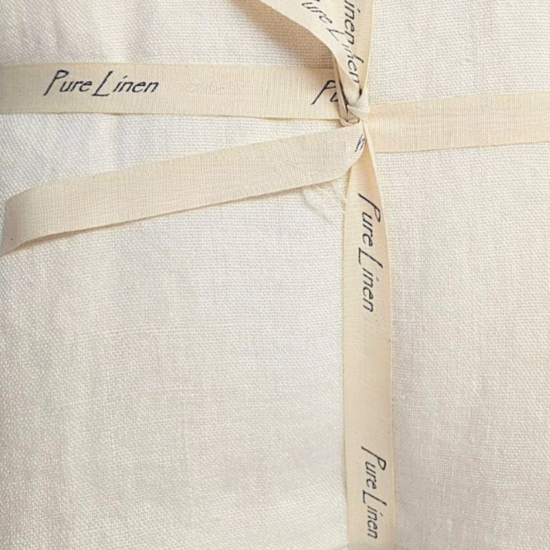 A close-up of a cream-colored linen quilt with a matching ribbon tied in a bow. The ribbon is printed with the words 'Pure Linen' in black script.