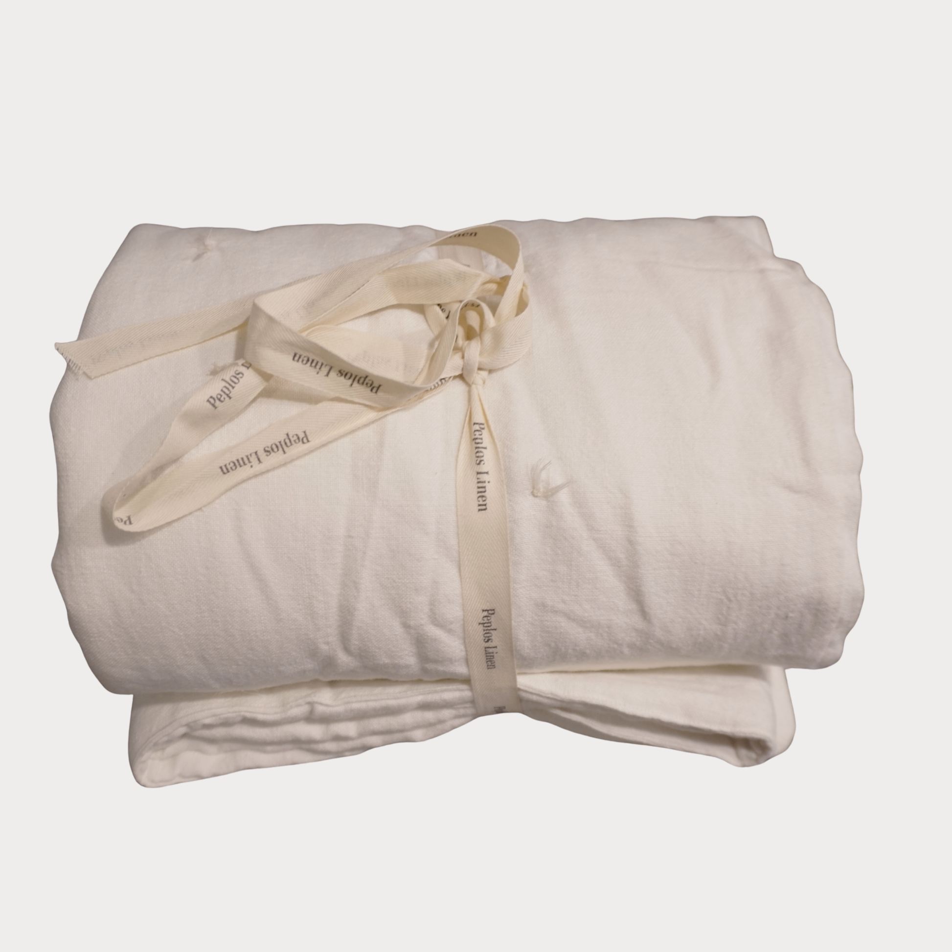 A folded white linen blanket tied with a cream-colored ribbon printed with the brand name 'Peplos Linen'.