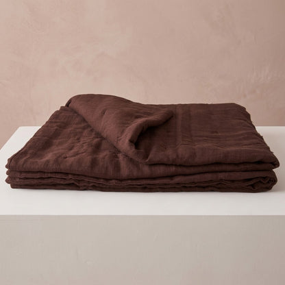 Chocolate brown linen quilt folded on a white surface, showing its soft, textured layers and relaxed drape.