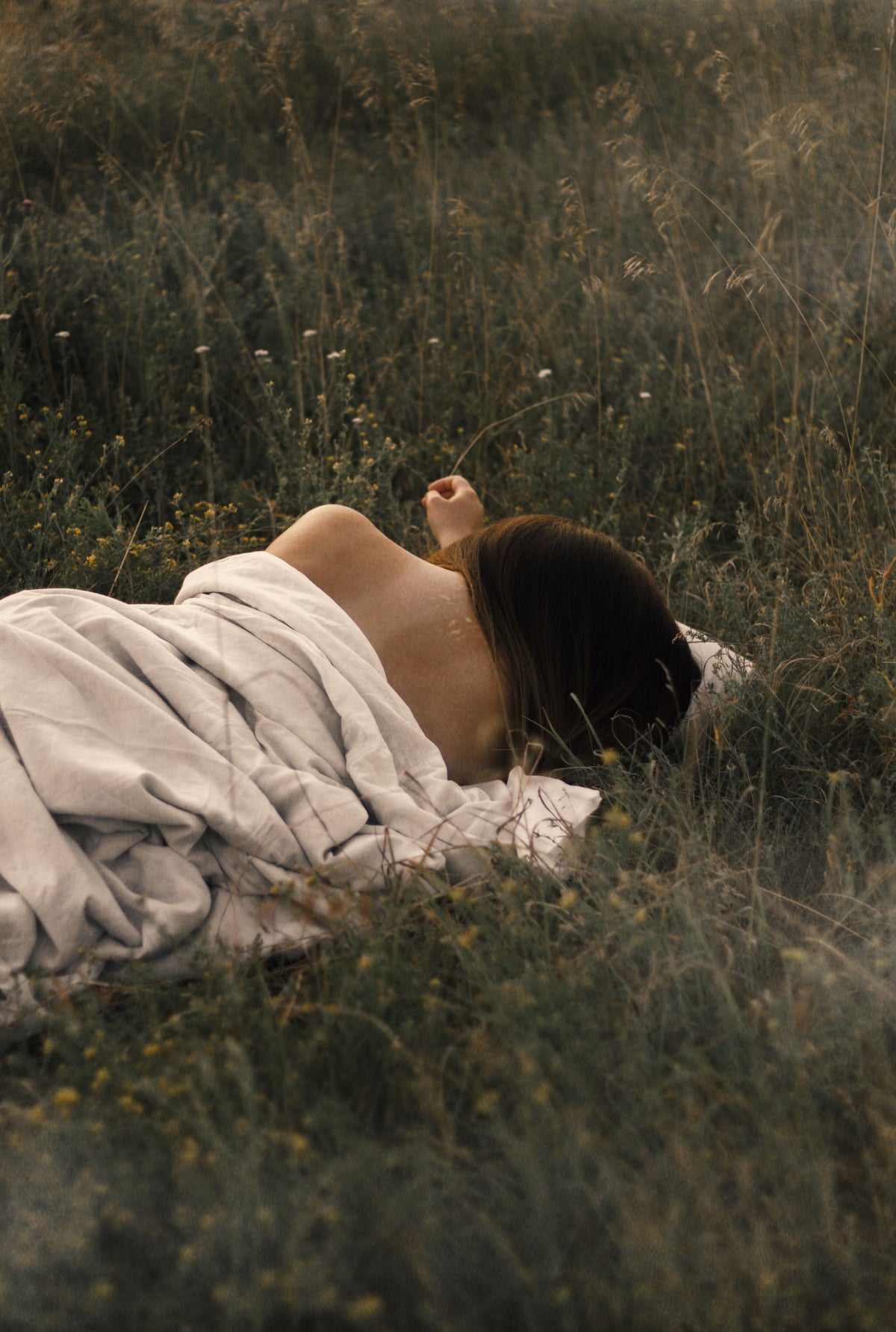 A woman wrapped in linen laying in garden filled with flowers and tall grass